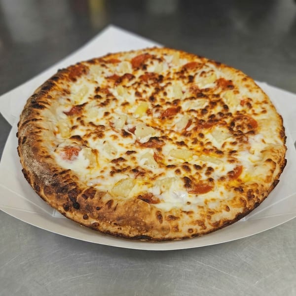 A whole pineapple and pepperoni pizza from The Clarksville Crust, on a white paper plate.