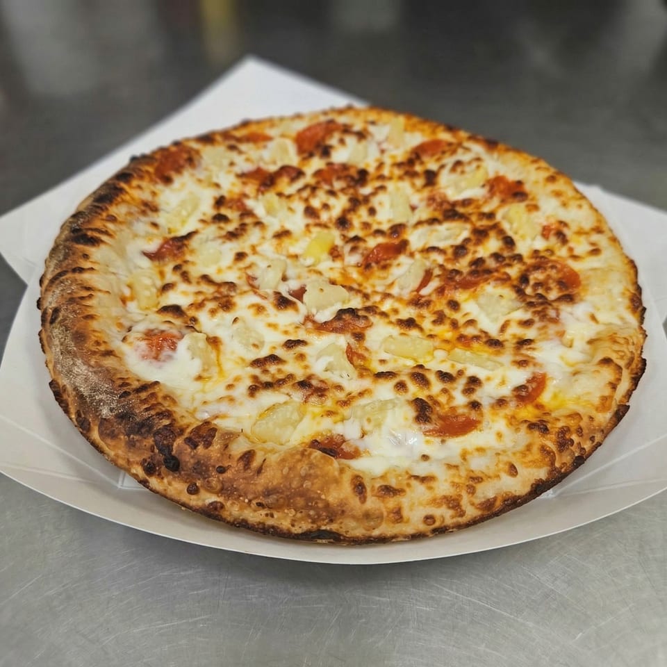 A whole pineapple and pepperoni pizza from The Clarksville Crust, on a white paper plate.