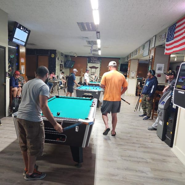 Patrons playing pool at The Clarksville Crust, with an American flag hanging on the wall.