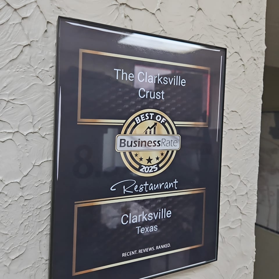 A framed "Best of BusinessRate 2025 Restaurant" award for The Clarksville Crust, mounted on a textured wall.