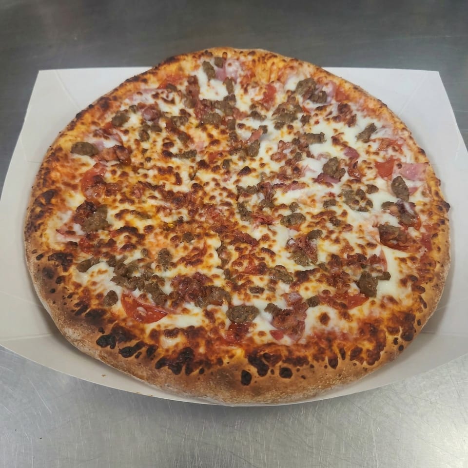 A whole Clarksville Crust pizza with melted cheese, sausage, and pepperoni on a white tray.
