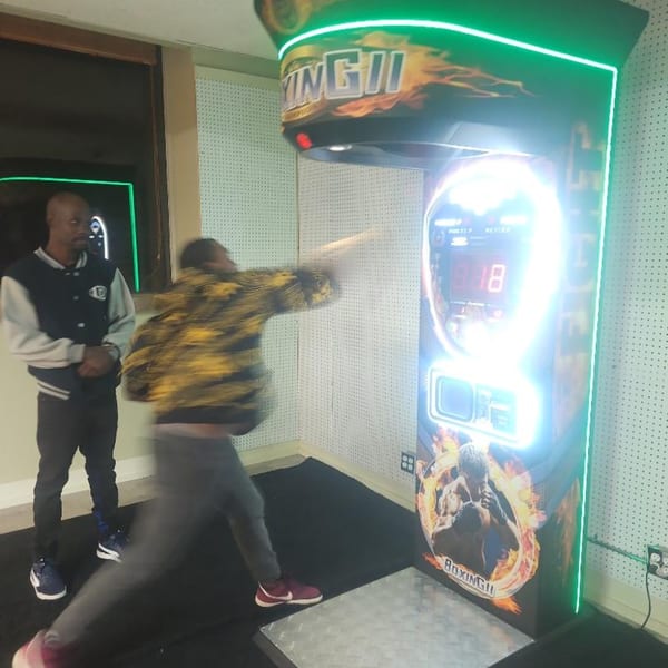 Two men playing a boxing arcade game, one mid-punch, at The Clarksville Crust.