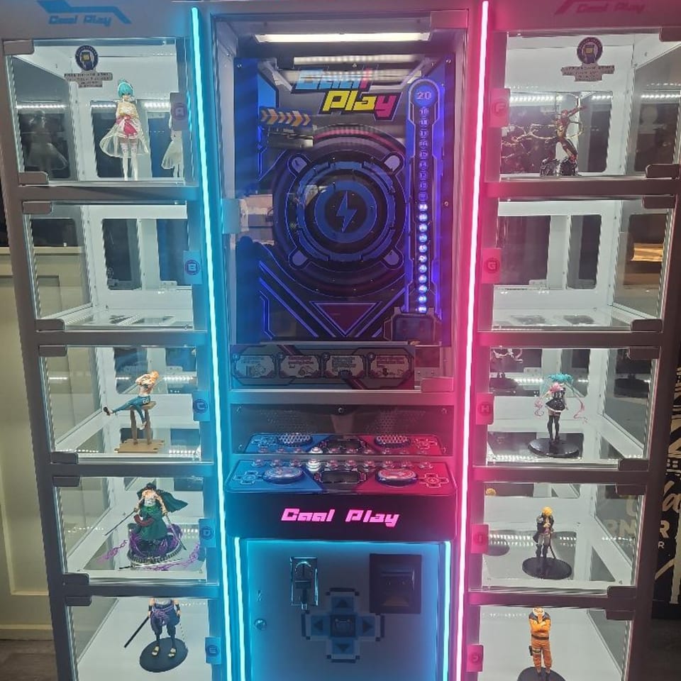 A brightly lit arcade game with anime figures displayed in glass cases on either side.