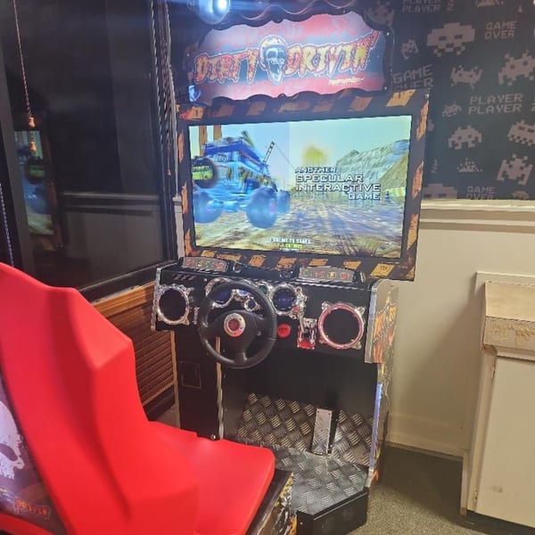A Dirty Driving arcade game with a red seat and steering wheel, set against a Space Invaders wallpaper.