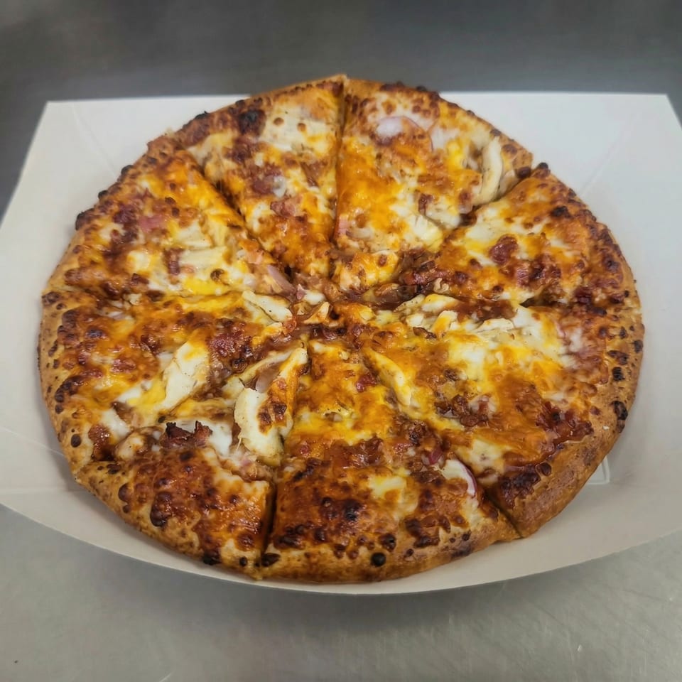 A whole pizza from The Clarksville Crust, topped with melted cheese and chicken, in a white box.