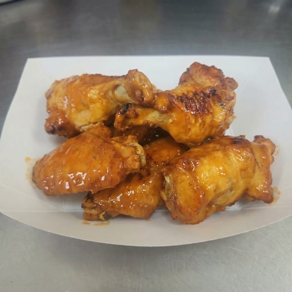A white paper tray filled with several golden-brown, saucy chicken wings from The Clarksville Crust.