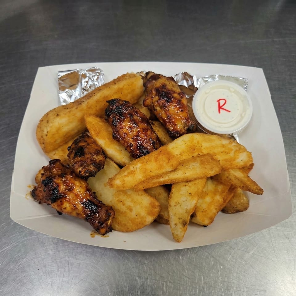 A white paper tray filled with crispy potato wedges and glazed chicken wings, with a side of ranch.
