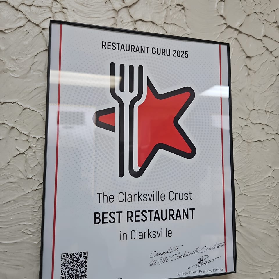 A framed "Restaurant Guru 2025 Best Restaurant" award for The Clarksville Crust hangs on a textured wall.