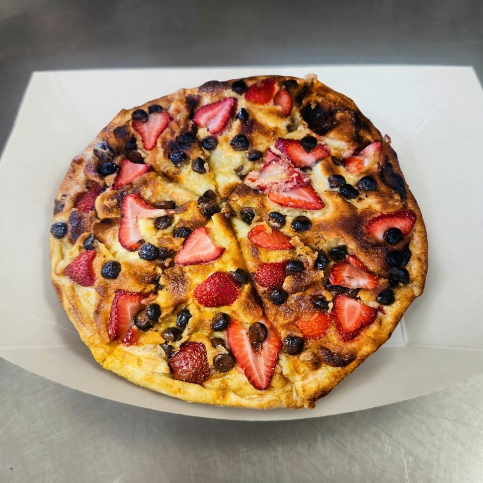 A dessert pizza from The Clarksville Crust, topped with sliced strawberries and chocolate chips.