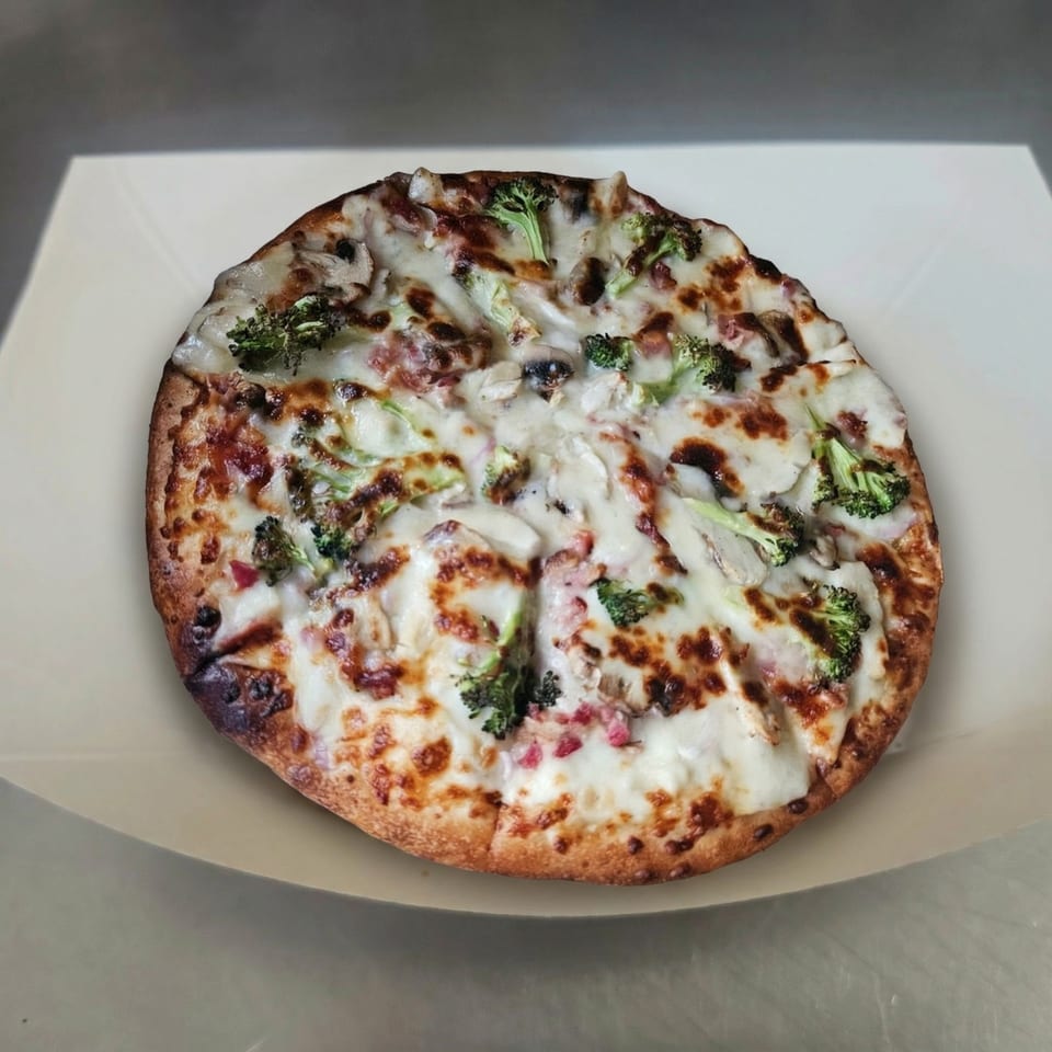 A freshly baked pizza from The Clarksville Crust, topped with melted cheese, broccoli, and mushrooms.