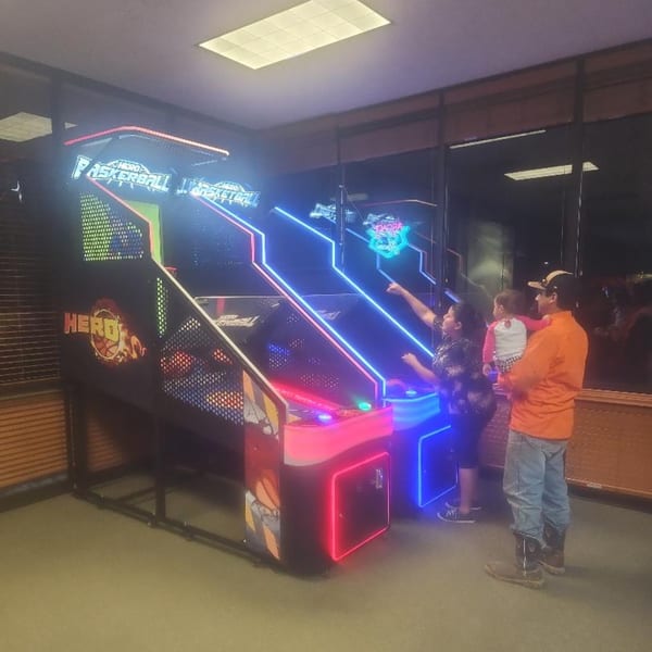 Family playing arcade basketball at The Clarksville Crust, with bright neon lights illuminating the game.