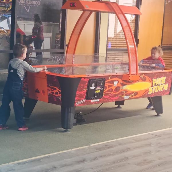 Two young children playing air hockey on a red "Fire Storm" table at The Clarksville Crust.
